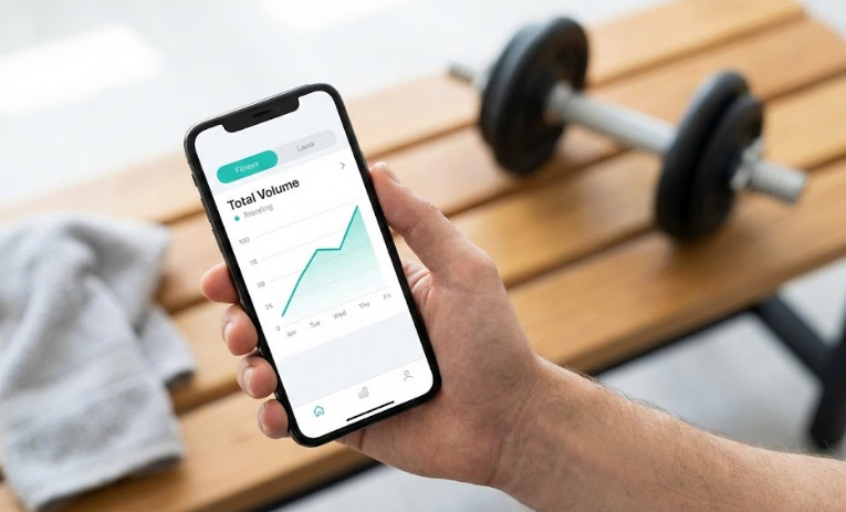 筋トレの総負荷量をスマートフォンアプリのグラフで管理し、漸進性過負荷を実践するイメージ画像。
